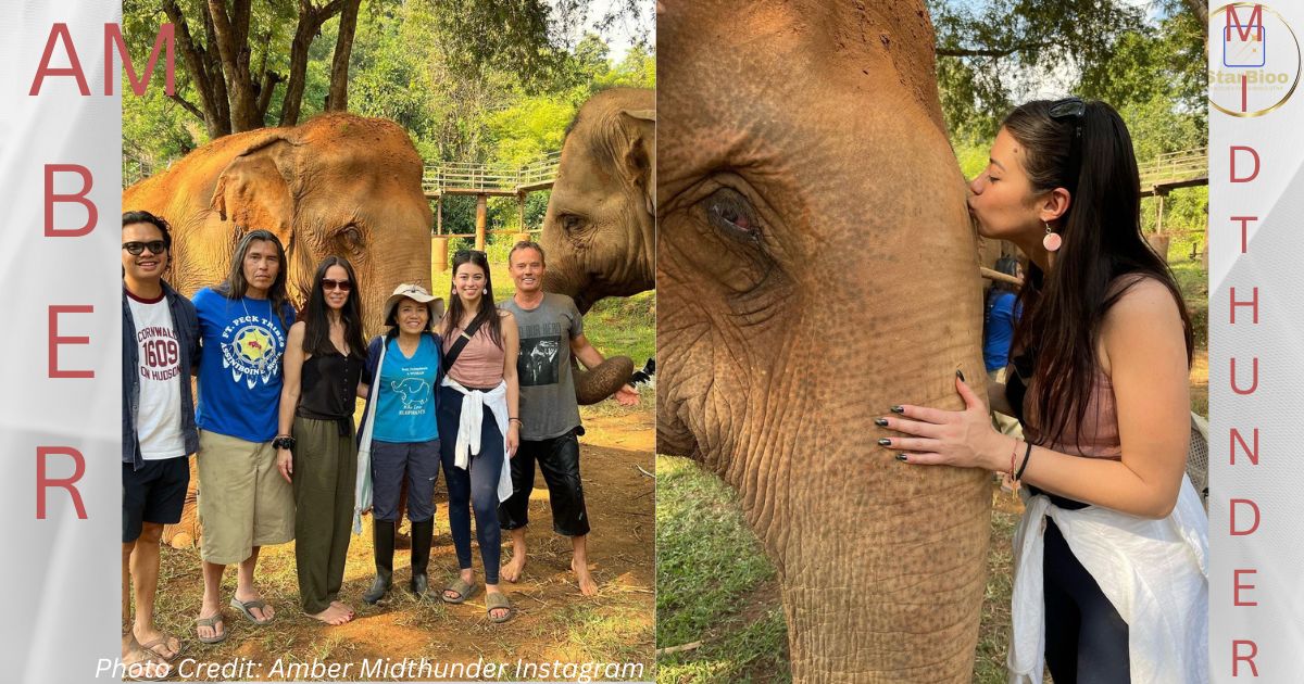 Amber Midthunder is seen kissing an elephant while visiting with the Prey team. The photo shows Midthunder wearing a pink top and jeans, standing in front of the elephant with the rest of the team. The visit was likely part of the film's promotion or a break from filming.