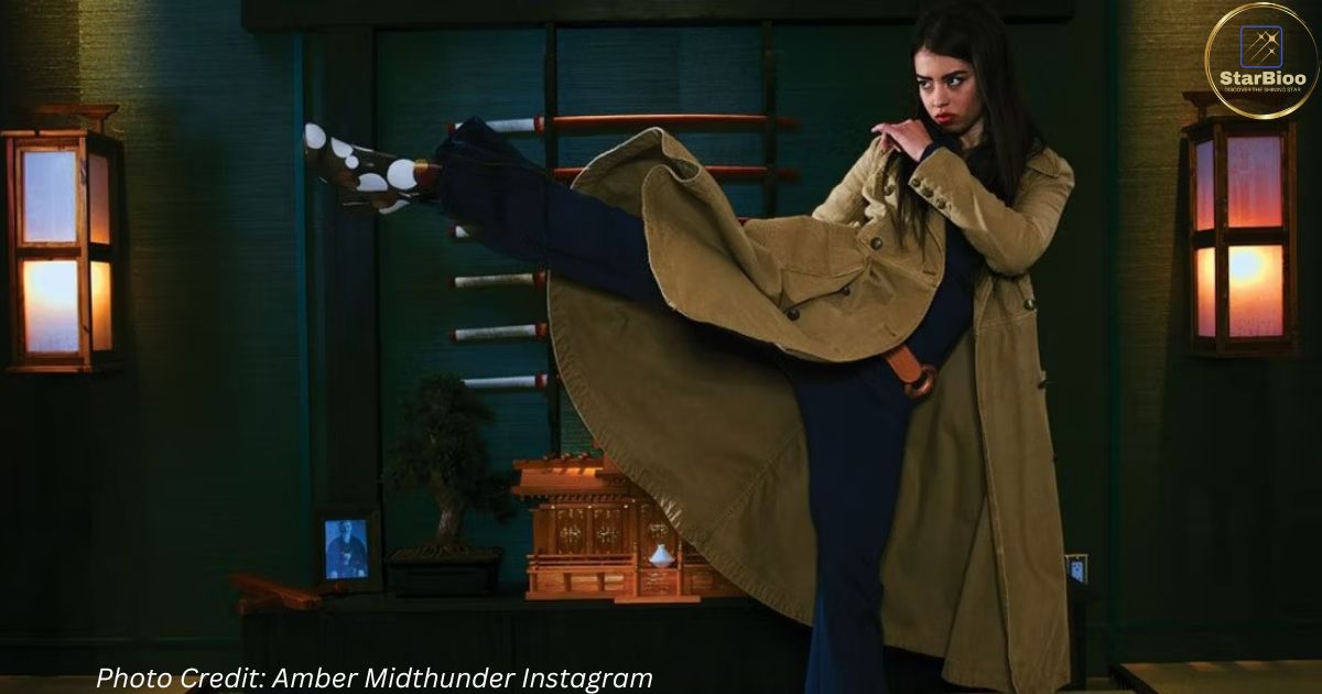 Amber Midthunder is seen in a still from a movie/TV series wearing a brown jacket and black pants, showing off her action moves. The photo captures Midthunder in a dynamic pose, with a serious expression on her face. The specific movie/TV series is not mentioned in the search results, but Midthunder is known for her action roles, including her performance as Naru in the 2022 film "Prey."