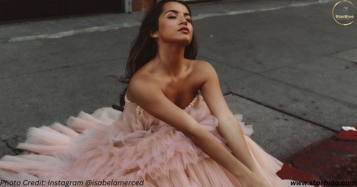 Isabela Merced looking gorgeous in a pink dress. She is sitting on the road and breathing the air with close eyes. she is wearing a pink dress.